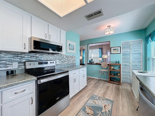 kitchen featuring appliances with stainless steel finishes, light wood-style flooring, visible vents, and white cabinetry