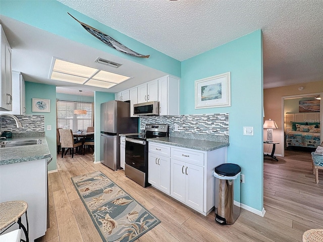 kitchen featuring visible vents, white cabinets, stainless steel appliances, light wood-type flooring, and a sink