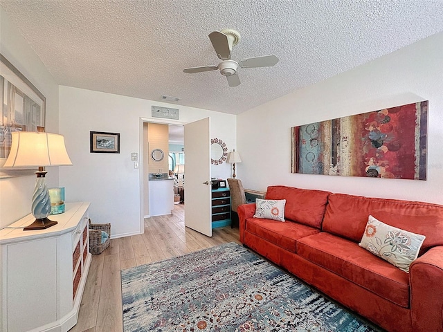 living area featuring a ceiling fan, visible vents, light wood-style flooring, and a textured ceiling