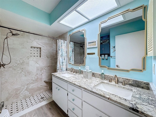 full bath featuring double vanity, a tile shower, a sink, and wood finished floors