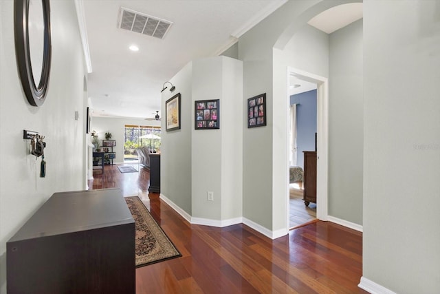 hall with arched walkways, wood finished floors, visible vents, baseboards, and ornamental molding