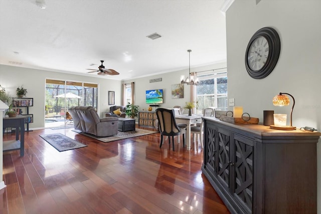 living room with baseboards, visible vents, dark wood-style flooring, crown molding, and ceiling fan with notable chandelier