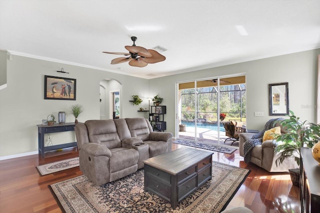 living room featuring arched walkways, baseboards, a ceiling fan, wood finished floors, and crown molding