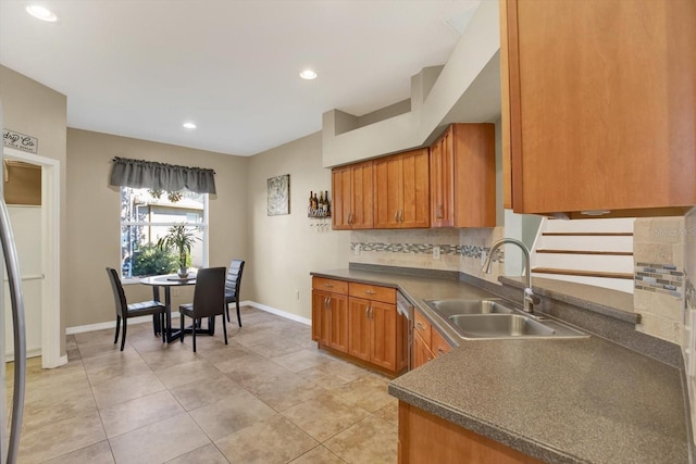 kitchen with tasteful backsplash, brown cabinetry, dark countertops, and a sink