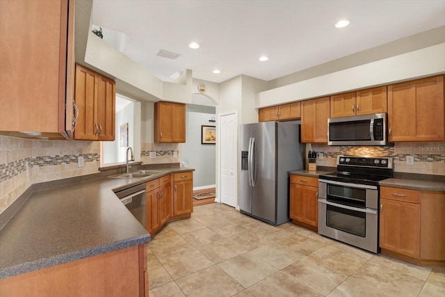 kitchen featuring dark countertops, decorative backsplash, appliances with stainless steel finishes, brown cabinetry, and a sink