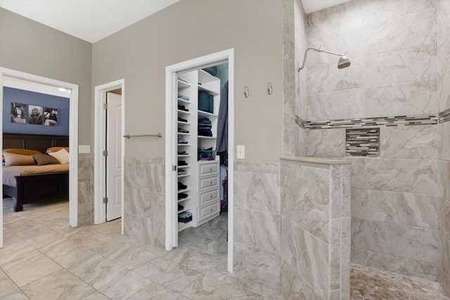 ensuite bathroom featuring ensuite bath, marble finish floor, a walk in closet, walk in shower, and tile walls