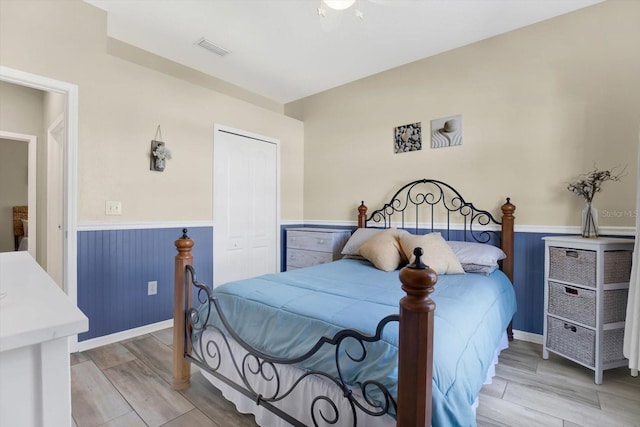 bedroom featuring light wood-style floors, a closet, a wainscoted wall, and visible vents