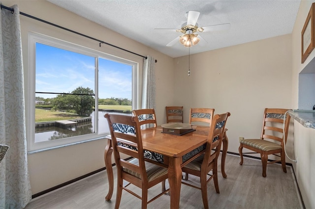 dining space featuring ceiling fan, light hardwood / wood-style floors, a textured ceiling, and a water view