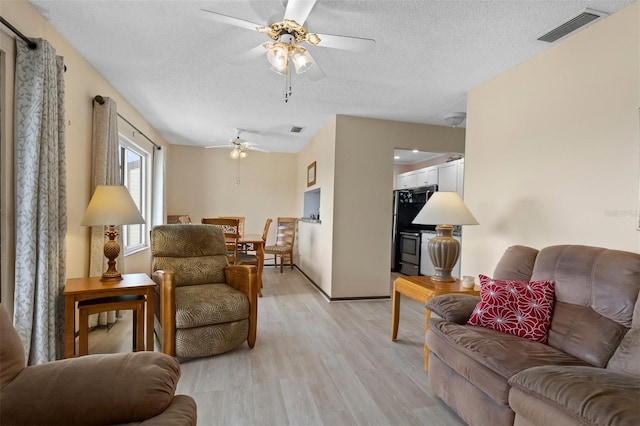 living room featuring ceiling fan, a textured ceiling, and light wood-type flooring