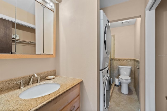 bathroom with toilet, tile walls, vanity, stacked washing maching and dryer, and tile patterned flooring