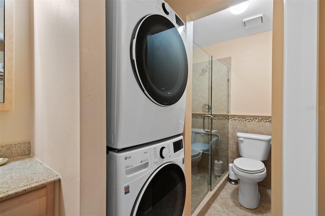 washroom featuring stacked washer and dryer, tile walls, and light tile patterned floors