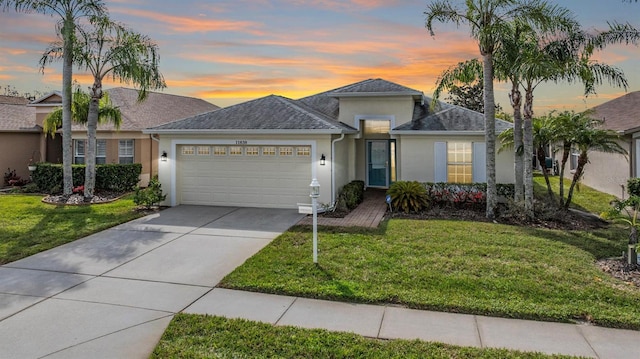 ranch-style home with stucco siding, an attached garage, a lawn, and driveway