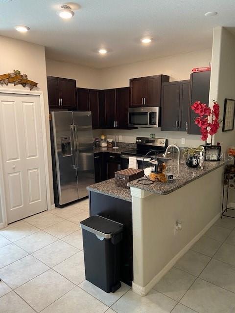 kitchen featuring dark brown cabinetry, kitchen peninsula, dark stone counters, and appliances with stainless steel finishes