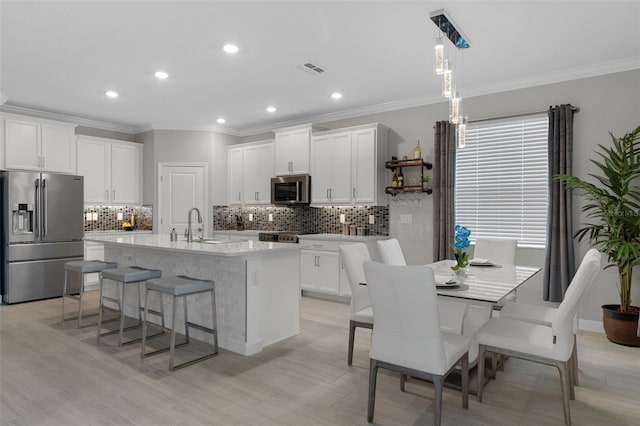 kitchen with a breakfast bar area, a center island with sink, light countertops, appliances with stainless steel finishes, and white cabinetry