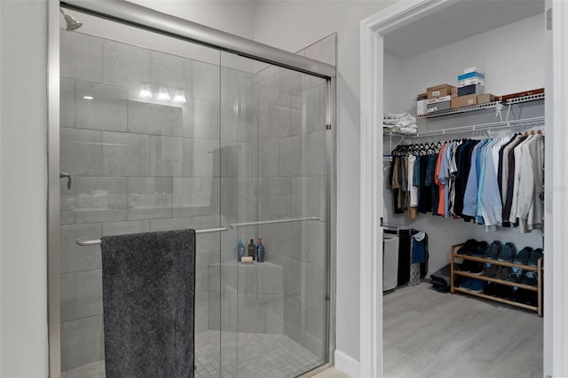 bathroom with a walk in closet, wood finished floors, and a shower stall