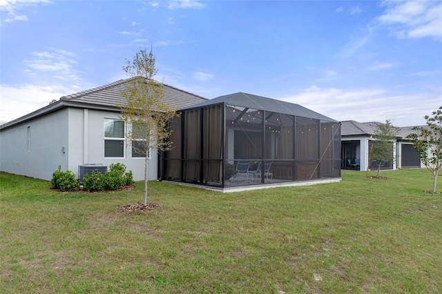 back of property with stucco siding, a lawn, and a lanai