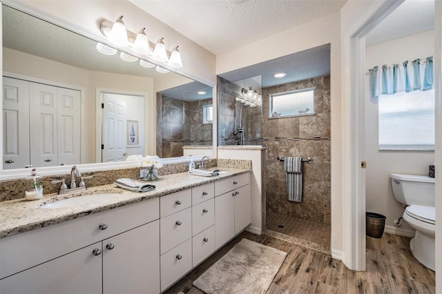 bathroom with toilet, a textured ceiling, a tile shower, vanity, and hardwood / wood-style flooring