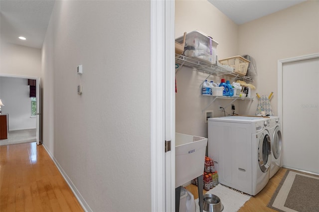 clothes washing area with washing machine and dryer, light wood-style flooring, laundry area, a sink, and baseboards