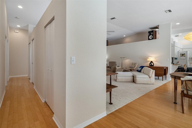 corridor with vaulted ceiling, light wood finished floors, and visible vents