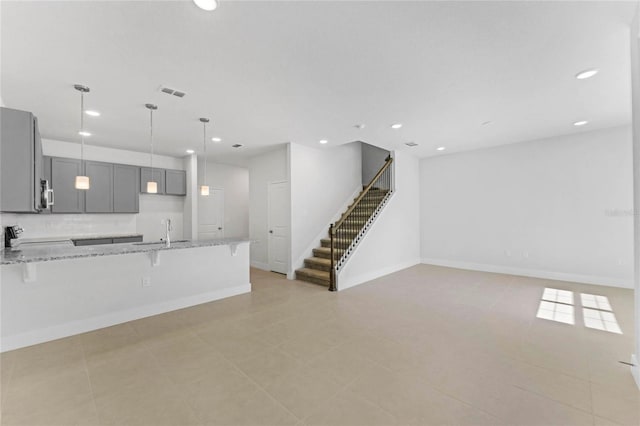 kitchen with a kitchen bar, sink, backsplash, gray cabinetry, and light stone countertops