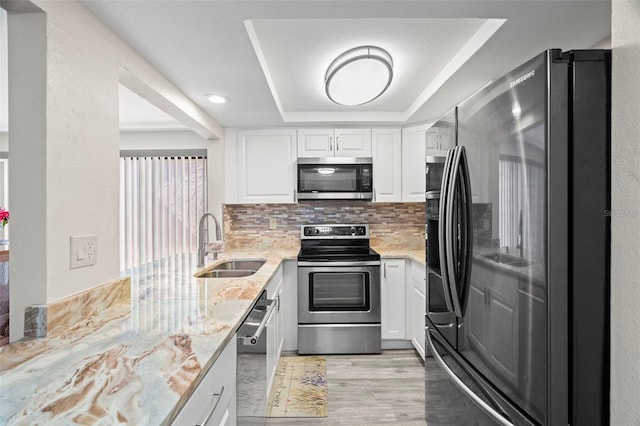 kitchen with a raised ceiling, white cabinetry, sink, stainless steel appliances, and light stone countertops