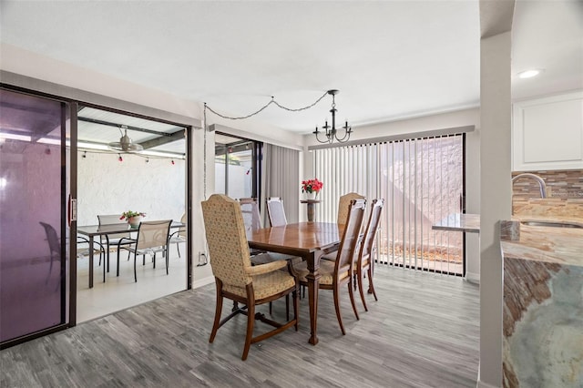 dining area with ceiling fan with notable chandelier, sink, and light wood-type flooring