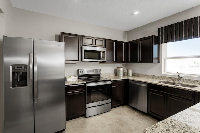 kitchen featuring dark brown cabinetry, appliances with stainless steel finishes, sink, and light stone counters