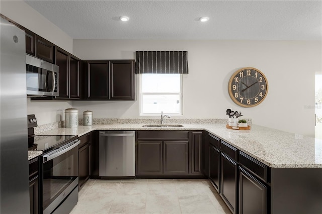 kitchen featuring appliances with stainless steel finishes, sink, light stone counters, kitchen peninsula, and a textured ceiling