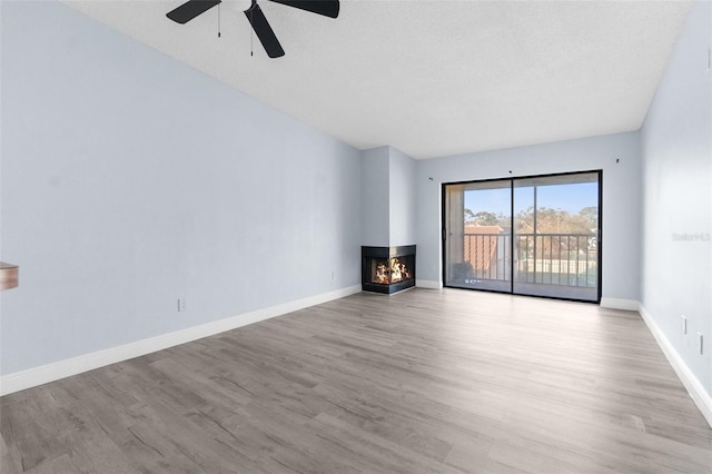 unfurnished living room with ceiling fan, a multi sided fireplace, a textured ceiling, and light hardwood / wood-style flooring