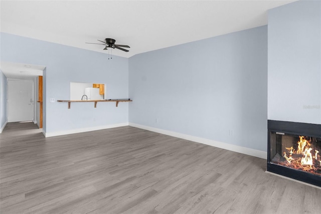 unfurnished living room featuring a multi sided fireplace, hardwood / wood-style floors, and ceiling fan