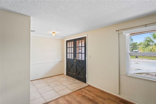 entryway featuring light wood-type flooring, visible vents, wainscoting, and a textured ceiling