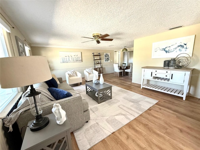 living area featuring light wood-type flooring, visible vents, ceiling fan, and a textured ceiling