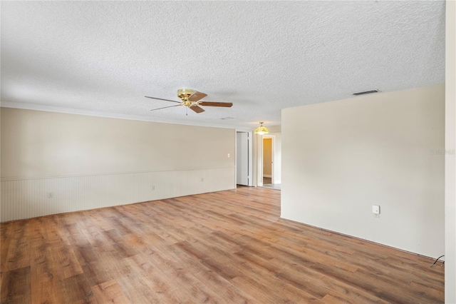 spare room with a textured ceiling, ceiling fan, visible vents, wainscoting, and light wood finished floors