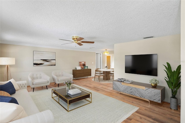 living area featuring a textured ceiling, wood finished floors, visible vents, and a ceiling fan