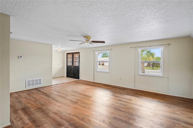 spare room featuring a textured ceiling, light wood-style flooring, plenty of natural light, and visible vents