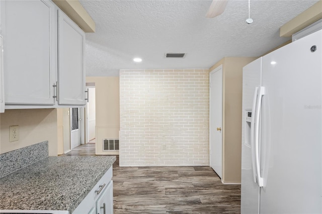 kitchen with white fridge with ice dispenser, white cabinets, visible vents, and light stone countertops