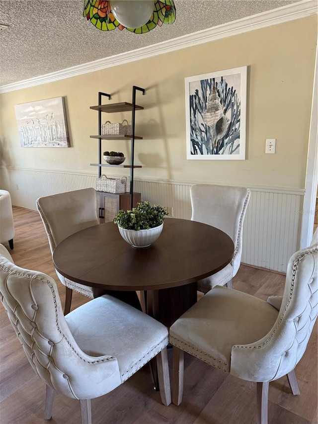 dining space featuring light wood finished floors, ornamental molding, a textured ceiling, and wainscoting