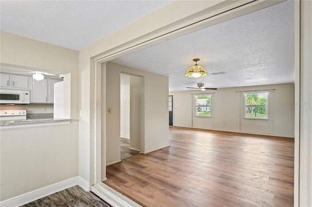 interior space featuring light wood-style floors, baseboards, a ceiling fan, and a textured ceiling