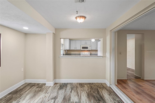 kitchen with white microwave, wood finished floors, baseboards, white cabinets, and light countertops