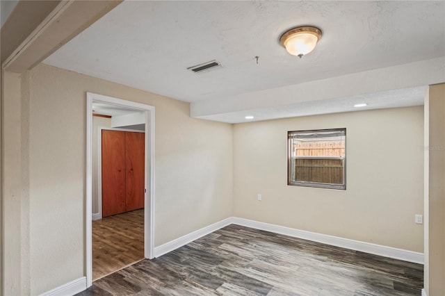 unfurnished room featuring a textured ceiling, wood finished floors, visible vents, and baseboards