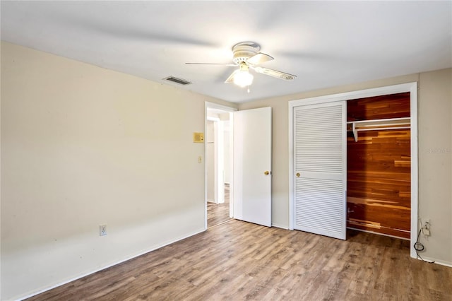 unfurnished bedroom with a closet, visible vents, a ceiling fan, wood finished floors, and baseboards