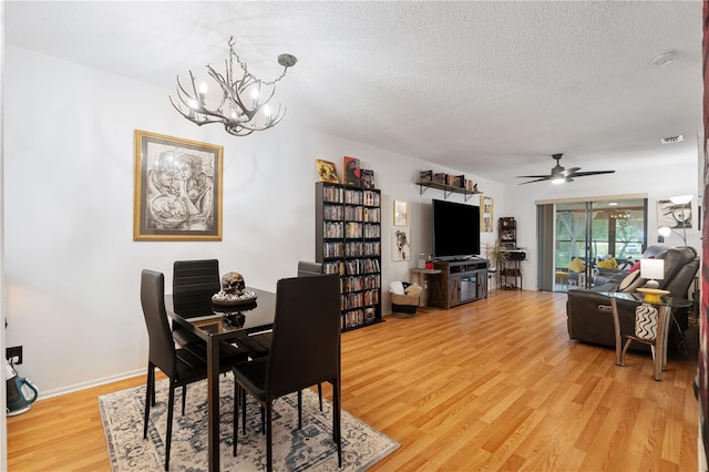 dining area featuring baseboards, light wood-style flooring, a textured ceiling, and ceiling fan with notable chandelier