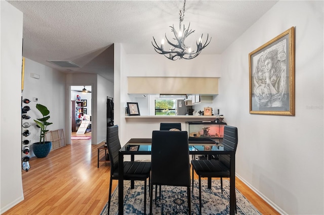 dining room featuring light wood finished floors, baseboards, a textured ceiling, and an inviting chandelier