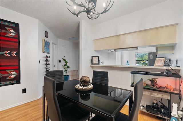 dining space featuring a textured ceiling, baseboards, wood finished floors, and a chandelier