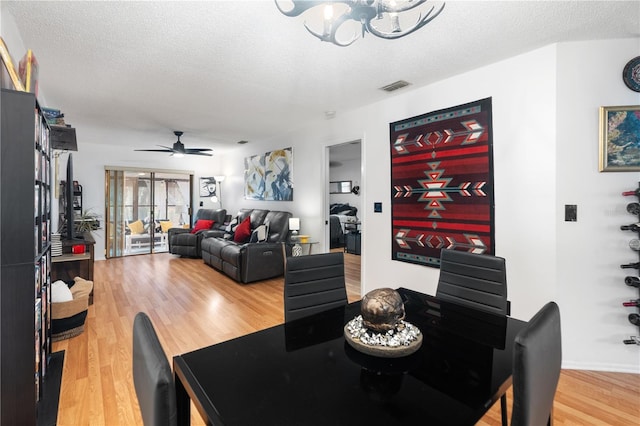 dining space with a textured ceiling, visible vents, wood finished floors, and ceiling fan with notable chandelier