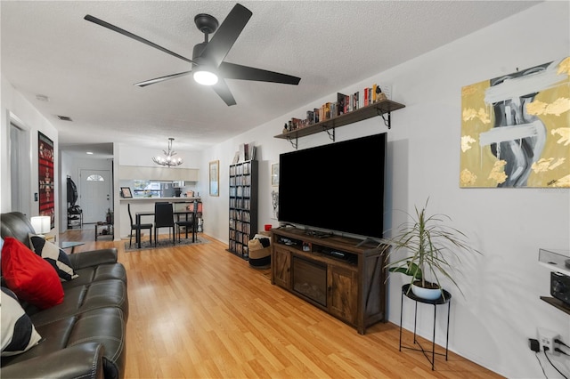 living room featuring light wood finished floors, visible vents, a textured ceiling, and ceiling fan with notable chandelier