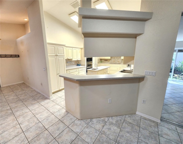 kitchen with visible vents, high vaulted ceiling, backsplash, cream cabinets, and light tile patterned flooring