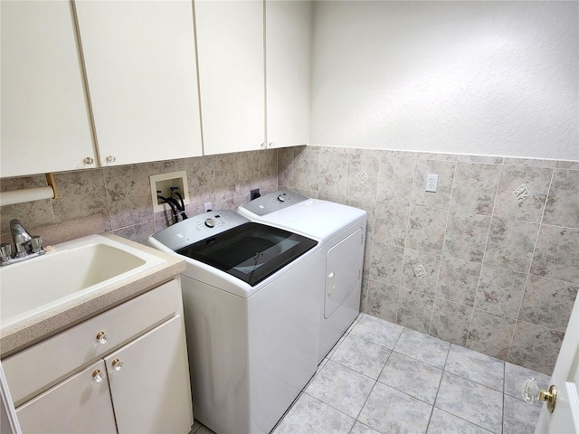 laundry room featuring washing machine and clothes dryer, light tile patterned floors, cabinet space, tile walls, and a sink