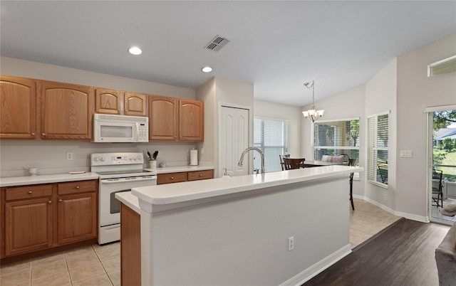 kitchen with pendant lighting, light tile patterned floors, white appliances, and an island with sink