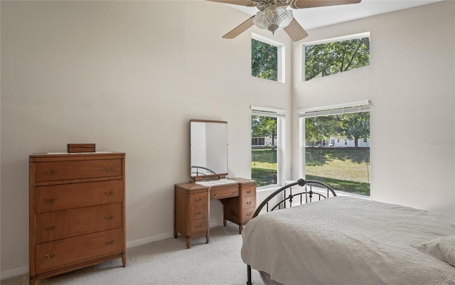 carpeted bedroom with multiple windows, a towering ceiling, and ceiling fan